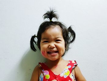 Portrait of cute smiling baby girl with pigtails against wall