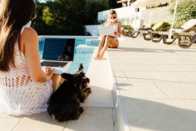 Women using laptop sitting by pool