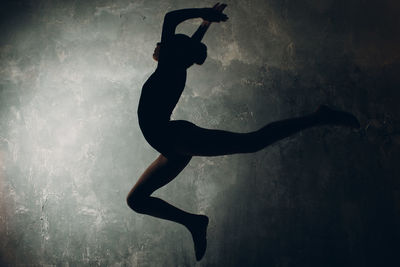 Silhouette girl jumping against wall