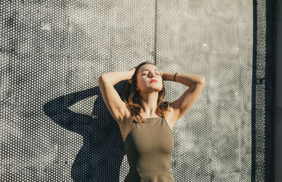 Thoughtful young woman with eyes closed while standing against warehouse