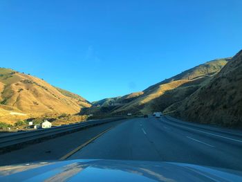 Road amidst mountains against clear blue sky seen through car windshield