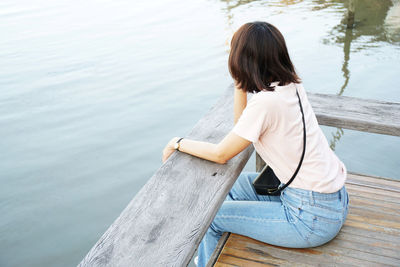 Rear view of woman sitting on pier over sea