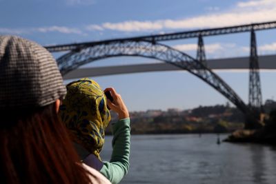 Friends photographing bridge and river against sky