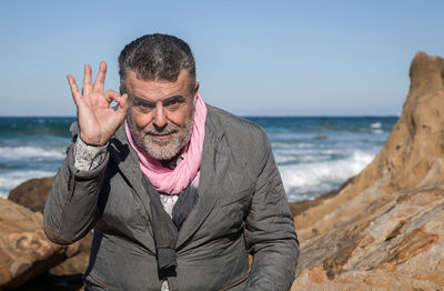 Portrait of mature man gesturing ok sign at beach