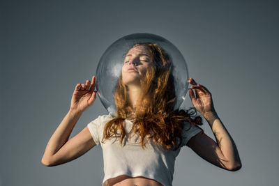 Low angle view of young woman wearing glass helmet in head against gray background