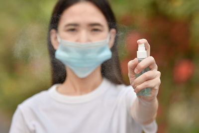 Portrait of young woman wearing mask holding hand sanitizer outdoors