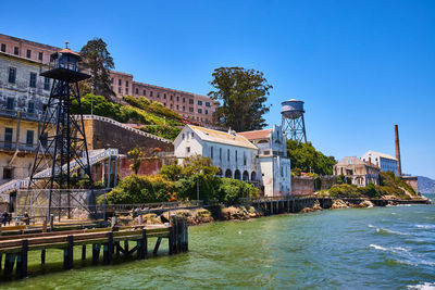 Buildings by sea against clear blue sky