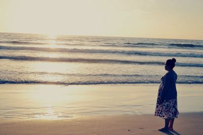 Rear view of woman standing at beach during sunset