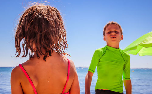 Rear view of siblings at beach against clear sky