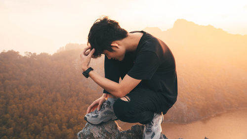 Young man using mobile phone against sunset sky