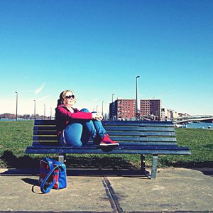 Rear view of woman sitting on bench against clear sky