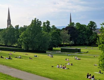 People in queen's park with buildings and trees against sky.