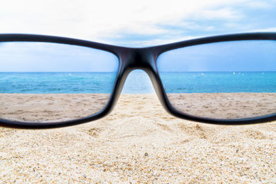 Close-up of sunglasses on beach against sky