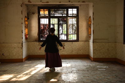 Rear view of woman standing on floor against window in building