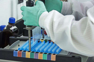 Cropped image of scientist pipetting sample from machine into test tubes