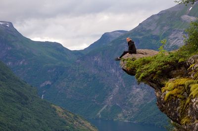 Full length of woman sitting on cliff against mountains