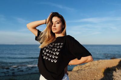 Young woman standing at beach against sky during sunset