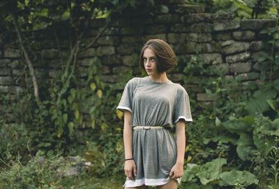 Portrait of young woman standing against plants and wall