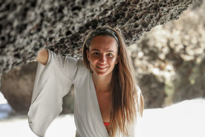 Portrait of smiling woman standing by rock formation in sea