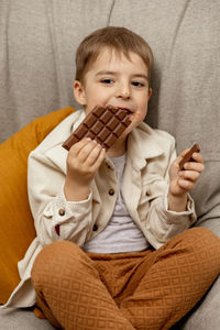 Little adorable boy sitting on the couch at home and eating chocolate bar. child and sweets