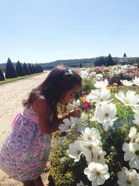 Side view of cute girl smelling cosmos flower against clear sky