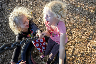 High angle view of happy sisters playing on tire swing at playground