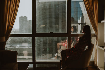 Side view of woman sitting on chair by window at home