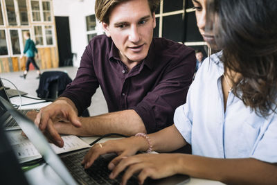 Confident male it professional discussing with female hacker using laptop at desk in creative office