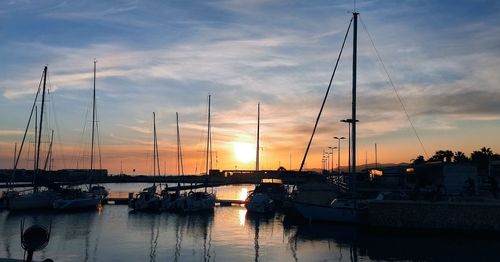 Sailboats moored at harbor during sunset