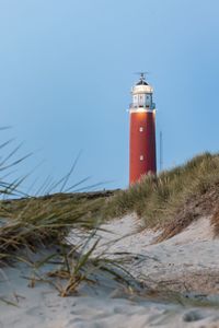 Lighthouse on beach by sea against sky