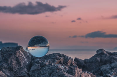 Crystal ball on rocky shore against sky during sunset