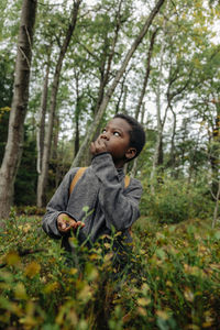 Boy looking up while eating berries near plants in forest