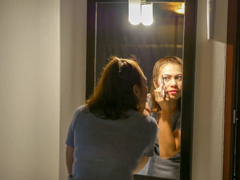 Rear view of woman applying makeup reflecting in mirror at home