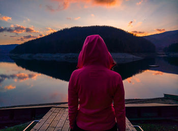 Rear view of mid adult woman standing on jetty over lake against sky during sunset