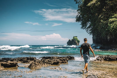 Rear view of man standing in sea against sky