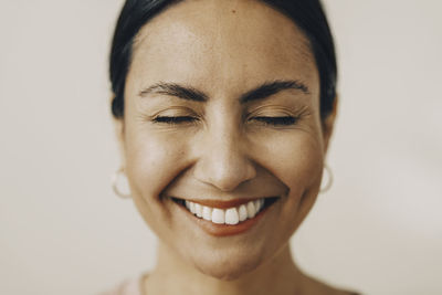Cheerful mid adult woman with eyes closed against white background