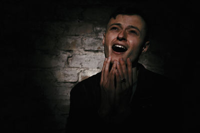 Young man yawning against wall at night