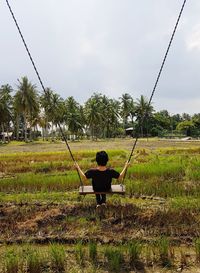 Rear view of man sitting on field against sky