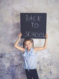 Portrait of smiling girl holding writing slate with text against wall