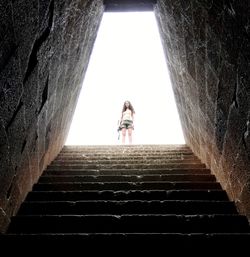 Low angle view of woman standing over steps seen through cave