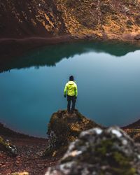 Rear view of man standing on rock by lake