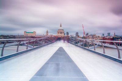 Digital composite image of bridge and buildings against cloudy sky