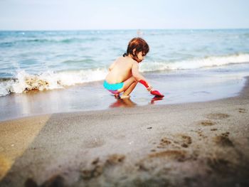 Full length of shirtless baby girl playing on shore at beach