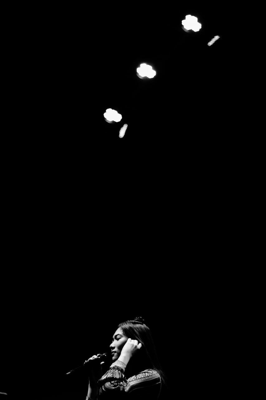 PORTRAIT OF MAN WITH ILLUMINATED LIGHTING EQUIPMENT IN DARK