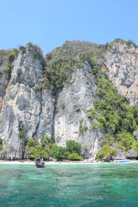 Scenic view of sea by mountain against clear blue sky