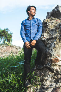 Low angle view of man standing on rock at grassy field against sky