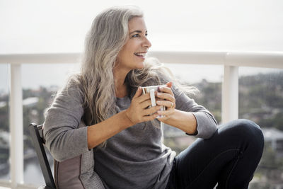 Thoughtful mature woman holding coffee mug while sitting on balcony