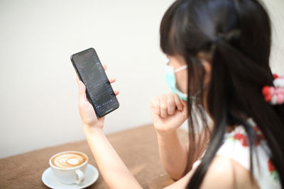 Woman wearing mask using mobile phone at table
