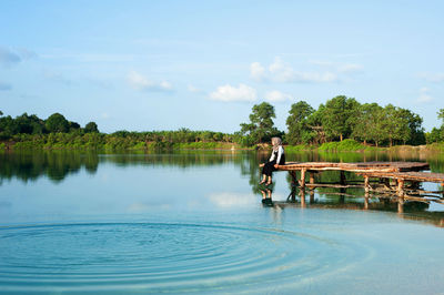 Woman sitting on pier over lake against sky