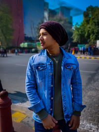 Young man looking away while standing on street in city